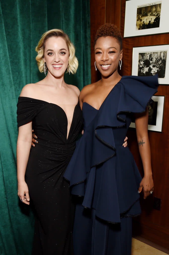 Two women smiling, one in a black off-shoulder dress, the other in a blue ruffled gown