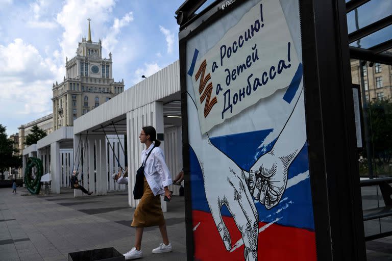 Una mujer pasa junto a un cartel en el que se lee "¡Por Rusia! Por los niños de Donbass!" con la letra Z, que se ha convertido en un símbolo de apoyo a la acción militar rusa en Ucrania, en el centro de Moscú el 11 de julio de 2022.