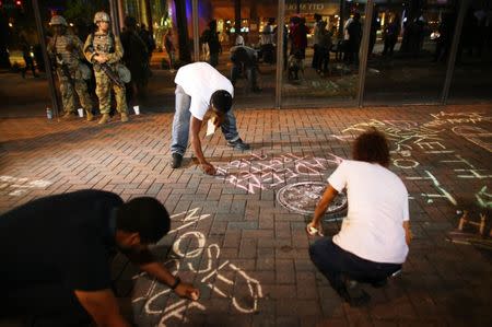 Protesters write the names of police shooting victims on the sidewalk while National Guard soldiers look on during another night of protests over the police shooting of Keith Scott in Charlotte, North Carolina, U.S. September 23, 2016. REUTERS/Mike Blake