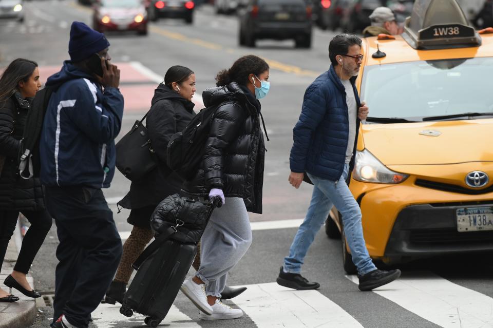 A woman wearing a face mask and gloves pulls her luggage as she walks through Manhattan on March 12, 2020 in New York City. - New York Governor Andrew Cuomo on March 12, 2020 banned public gatherings of more than 500 people, including shows in Manhattan's iconic Broadway theater district. Only schools, hospitals, nursing homes and mass transit facitilities are excepted from the rule -- which goes into effect for Broadway at 5:00 pm March 12, 2020, and 24 hours later everywhere else, Cuomo told journalists. (Photo by Angela Weiss / AFP) (Photo by ANGELA WEISS/AFP via Getty Images)