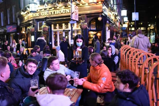 A waitress serves drinks as customers sit at tables set up outside pubs in Soho, in London, on the day some of England's third coronavirus lockdown restrictions were eased by the British government on April 12.