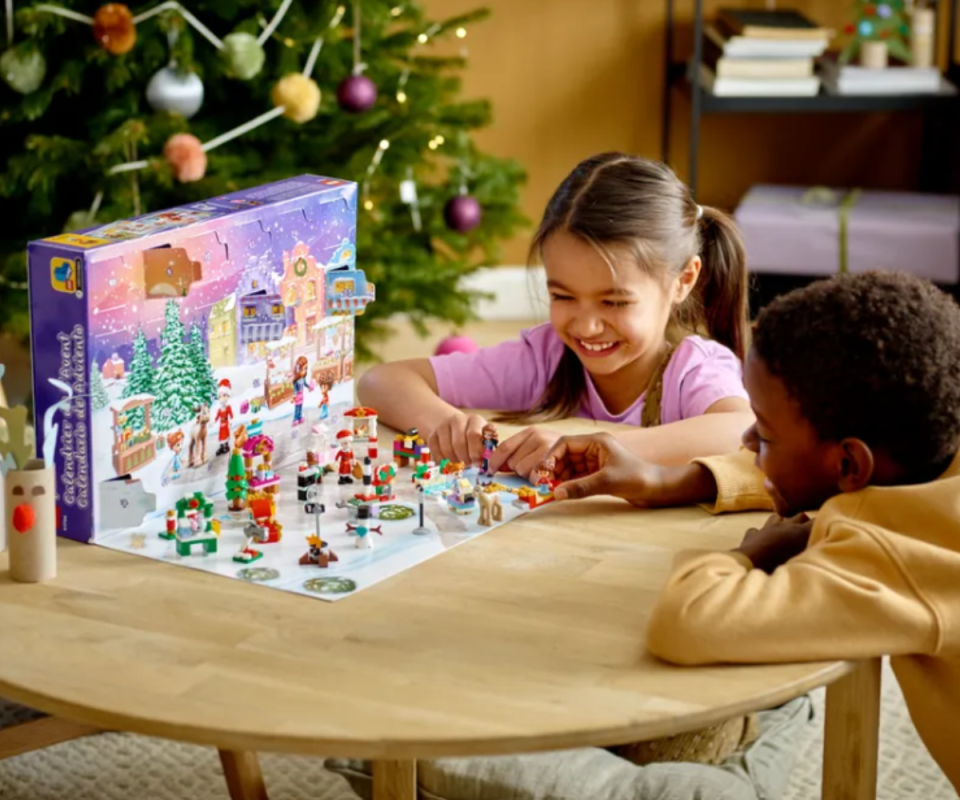 Two kids playing with the fold out of the Friends advent calendar on a wooden round table with a Christmas tree in the background.