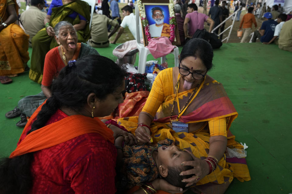 Kakarna Alkananda, a member of the Goud family, sticks out her tongue as she asks a child on her lap to keep her mouth open to receive a live fish stuffed with a herbal paste, in Hyderabad, India, Saturday, June 8, 2024. Every year thousands of asthma patients arrive here to receive this fish therapy from the Bathini Goud family, which keeps a secret formula of herbs, handed down by generations only to family members. The herbs are inserted in the mouth of a live sardine, or murrel fish, and slipped into the patient's throat. (AP Photo/Mahesh Kumar A.)