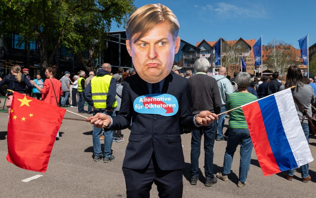 Demonstrator in mask depicting Maximilian Krah while holding Chinese and Russian flags with sign saying Alternative for Dictators