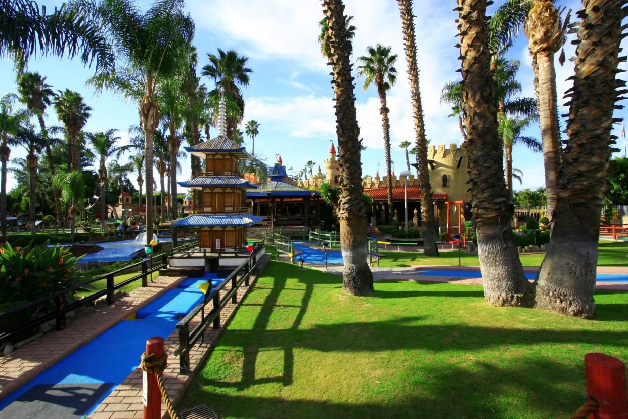A miniature golf course with a pagoda, palm trees and blue sky.