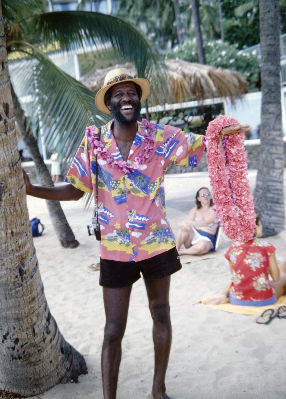 Wally Amos standing on a beach wearing a Hawaiian shirt and holding a lei