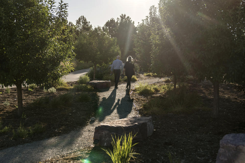 On Tuesday, Sept. 5, 2023, Lonnie Phillips, left, and his wife, Sandy, walk through a memorial garden in Aurora, Colo., for the victims killed and injured in the 2012 mass shooting at an Aurora movie theater. Sandy’s daughter, Jessica Ghawi, was among those killed. Suffering through their own personal loss, the couple set out to help other parents like them, traveling to shooting sites around the country. The trip continued for a decade. (AP Photo/David Goldman)