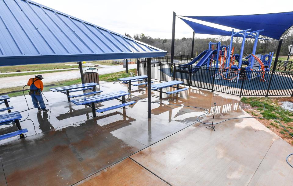 Workers clean the sidewalk area outside the new community playground, where there is scheduled a ribbon cutting 10 am on April 1 at Dolly Cooper Park in Powdersville, S.C.