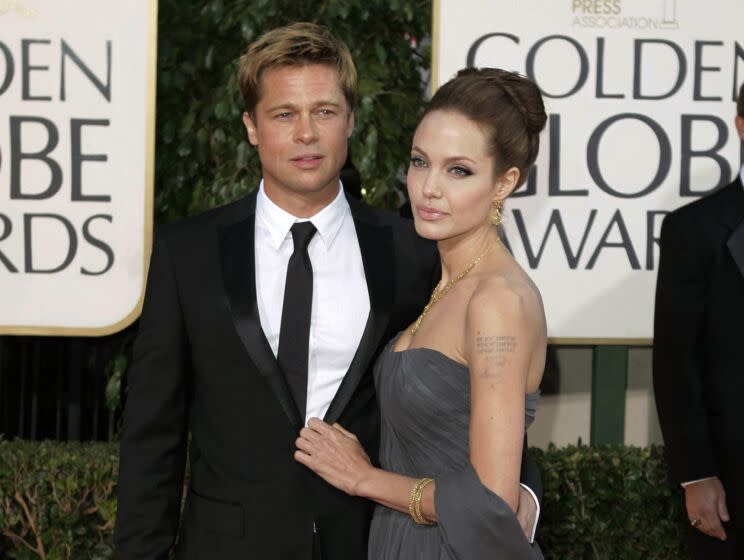 A man in a suit and a woman in a formal gown arrive on an awards show red carpet