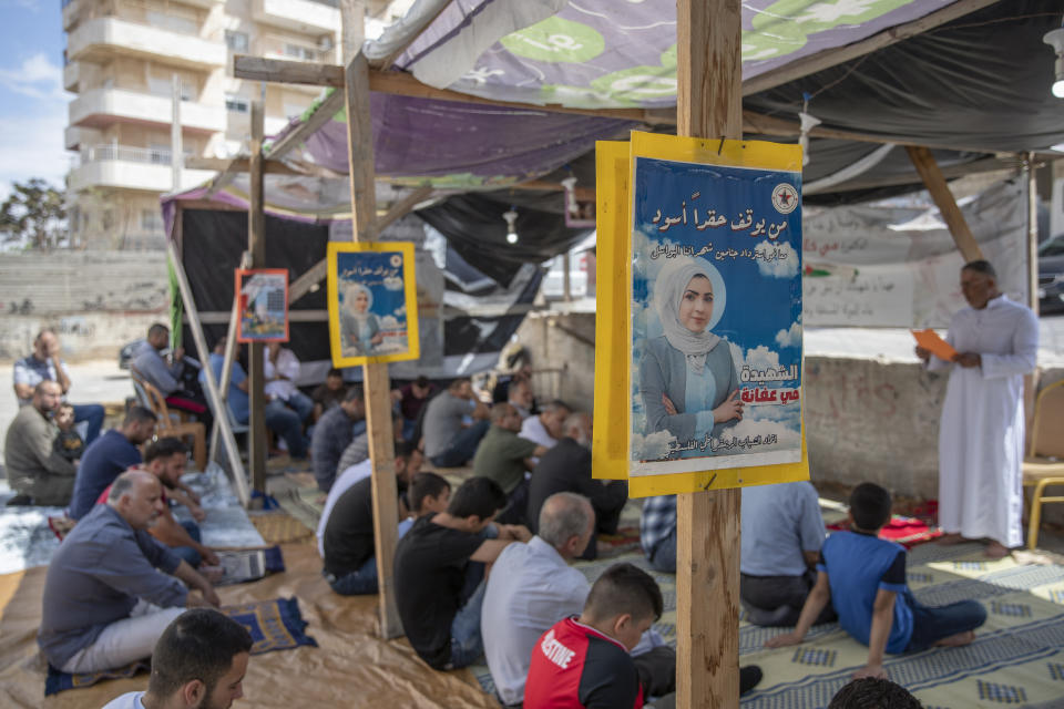 Palestinians attend Friday prayers under posters with picture and name of Mai Afaneh, who was shot dead by Israeli forces in the West Bank last June and held her body after, and reads "who can stop the dark grudge," at a sit-in tent for families of Palestinians killed in conflict and Israel is holding their bodies, in the village of Abu Dis, South of Ramallah, Friday, Sept. 24, 2021. (AP Photo/Nasser Nasser)