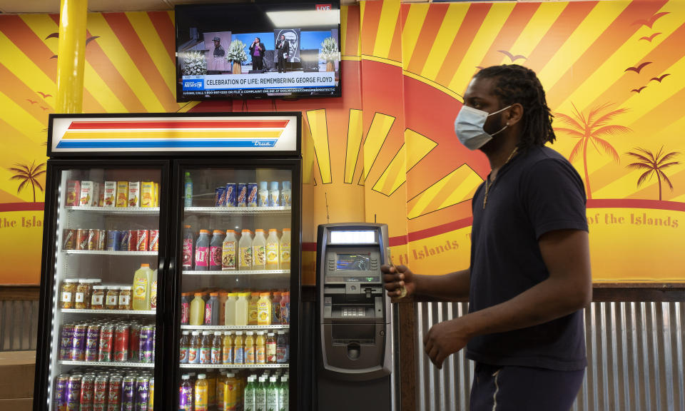 A customer waits in line at Golden Krust Caribbean restaurant, Tuesday, June 9, 2020, in Mount Vernon, N.Y. while the memorial service for George Floyd is carried on a television screen. Floyd died May 25 while in Minneapolis police custody. (AP Photo/Mark Lennihan)
