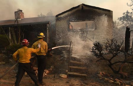 A firefighter sprays a smoldering home as the Erskine Fire burns near Weldon, California, U.S. June 24, 2016. REUTERS/Noah Berger