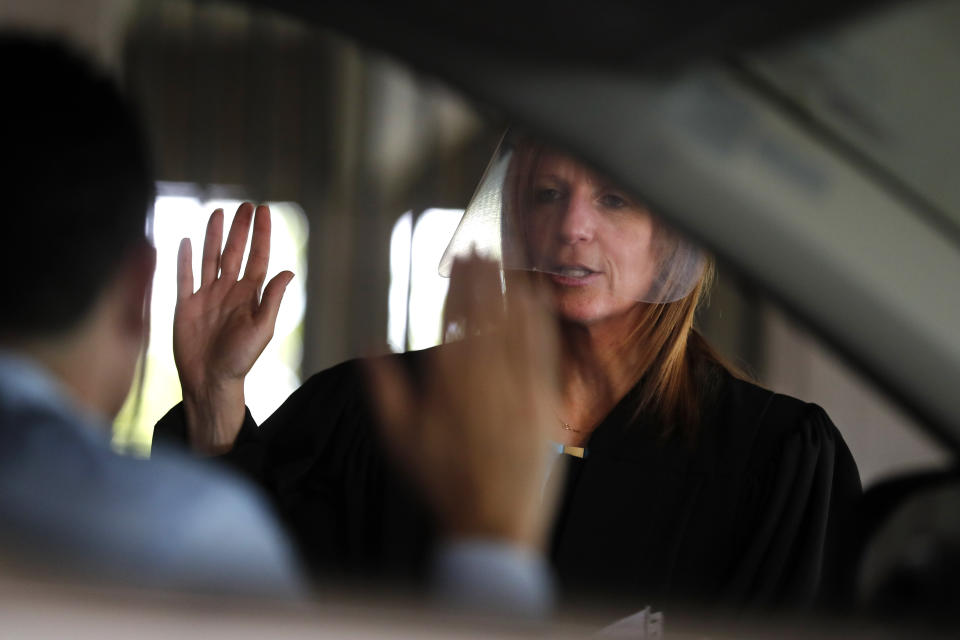 In this June 26, 2020 photo, U.S. District Judge Laurie Michelson administers the Oath of Citizenship to Ismael Gonzalez during a drive-thru naturalization service in a parking structure at the U.S. Citizenship and Immigration Services headquarters on Detroit's east side. The ceremony is a way to continue working as the federal courthouse is shut down due to Coronavirus. The U.S. has resumed swearing in new citizens but the oath ceremonies aren't the same because of COVID-19 and a budget crisis at the citizenship agency threatens to stall them again. (AP Photo/Carlos Osorio)