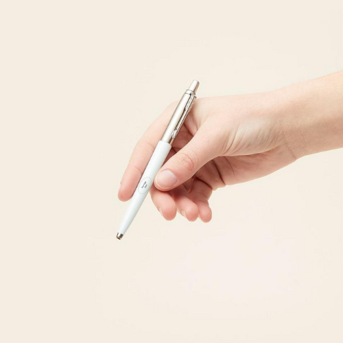 person holding white and silver merchery parker jotter pen against beige background