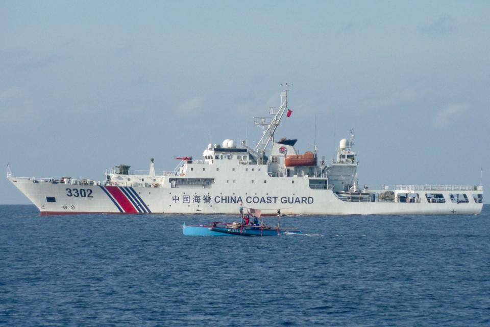 A small boat of Philippine fishermen sails past a larger Chinese coast guard ship near Scarborough Shoal in the South China Sea