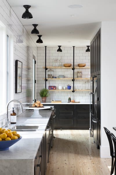 This kitchen in Austin, Texas, was designed by Royce Flournoy and expertly combines black, Shaker-style cabinets, white subway tiles, Carrera marble countertops, and wooden floors to create a balance between rustic warmth and industrial simplicity.