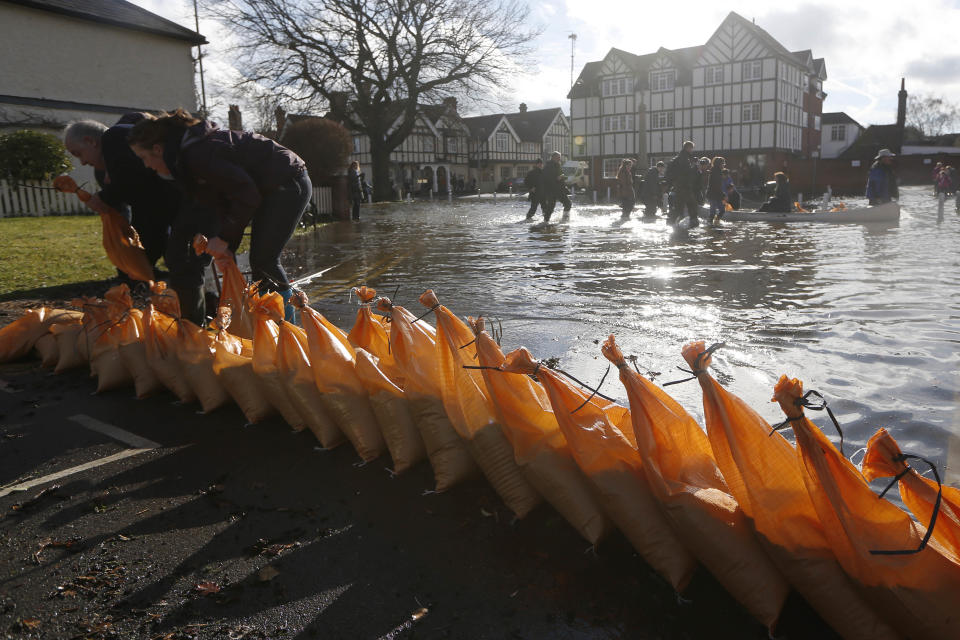 People build a defensive wall with sandbags on a flooded street, in Datchet, England, Monday, Feb. 10, 2014. The River Thames has burst its banks after reaching its highest level in years, flooding riverside towns upstream of London. Residents and British troops had piled up sandbags in a bid to protect properties from the latest bout of flooding to hit Britain. But the floods overwhelmed their defences Monday, leaving areas including the centre of the village of Datchet underwater. (AP Photo/Sang Tan)