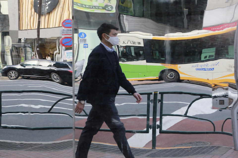 A man wearing face masks to protect against the spread of the coronavirus is reflected on mirrors on the wall of a tailor shop in Tokyo, Monday, Feb. 1, 2021. (AP Photo/Koji Sasahara)