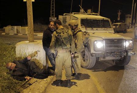 Israeli soldiers look at resting Palestinian passersby after the latter were prevented from crossing a road at the scene of a shooting attack near the West Bank city of Hebron April 14, 2014. REUTERS/Ammar Awad