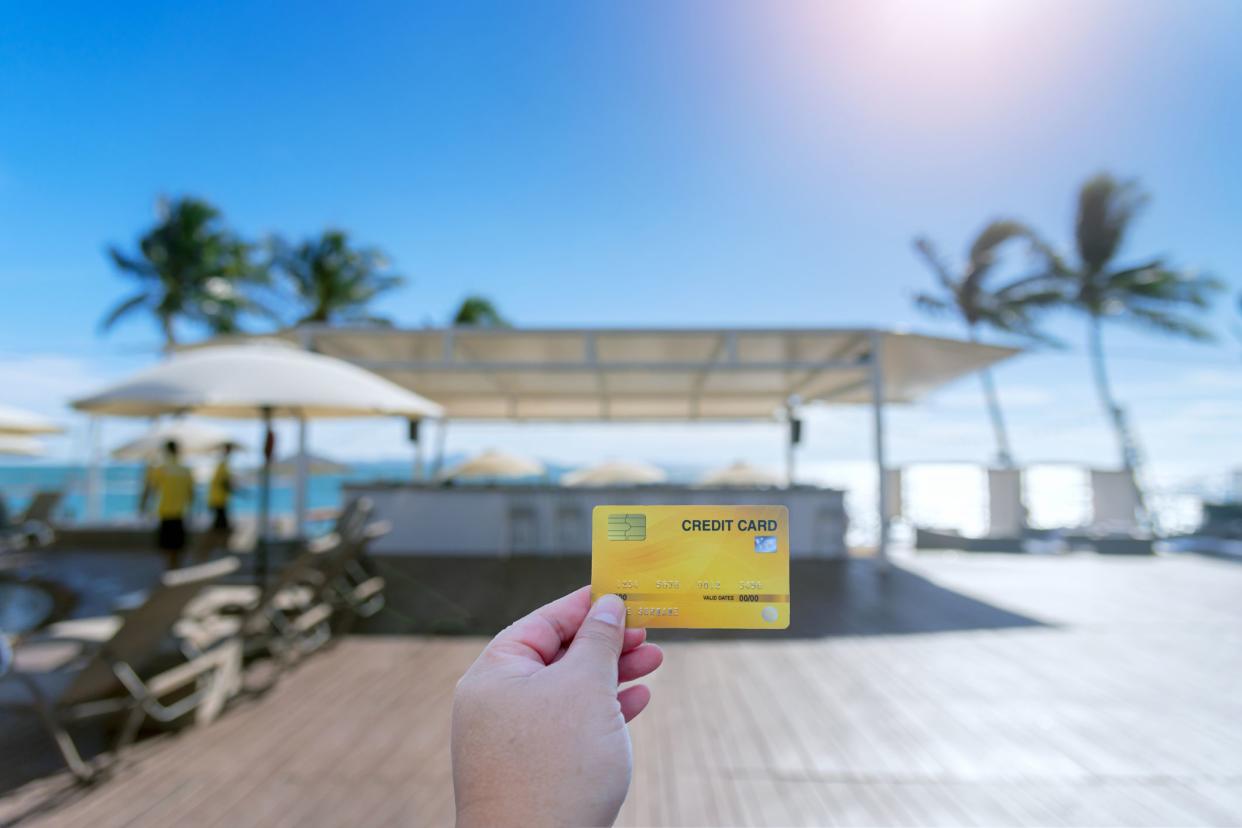 Hand holding credit card used for travel. Travel expenses credit card on holiday on blurred resort background. Travel on a small budget concept.