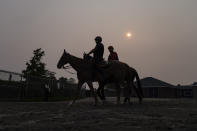 Haze from northern wildfires obscures the rising sun as horsemen ride their mounts towards the track ahead of the Belmont Stakes horse race, Wednesday, June 7, 2023, at Belmont Park in Elmont, N.Y. (AP Photo/John Minchillo)