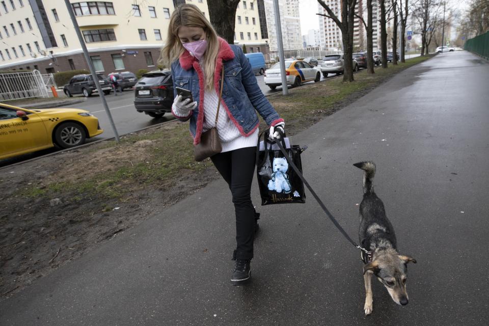 In this photo taken on Saturday, April 25, 2020, Anastasia Medvedeva, one of the organizers of the online adoption initiative called "Happiness Delivered At Home", wearing a face mask and gloves to protect from coronavirus, walks to meet with Alexandra Novatova, new owner in Moscow, Russia. Medvedeva said her project wants to make sure that the animals aren't adopted just as a temporary salve to the tedium and loneliness of lockdown. Moscow's coronavirus lockdown is bringing benefits to some of the city's dogs. With humans spending all day at home, it's an opportune period to find the time to acclimate a new dog and an online project is capitalizing on this to match shelter dogs with people. (AP Photo/Alexander Zemlianichenko)