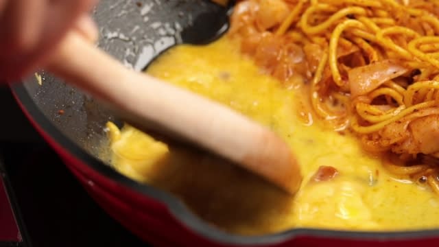 Scrambling eggs beside noodles in the same pan with wooden spatula