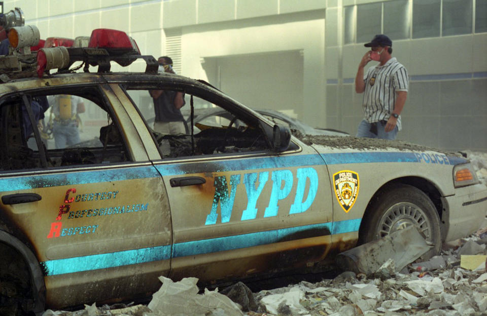 An NYPD officer stands by the wreckage of a police patrol vehicle. (Caters)