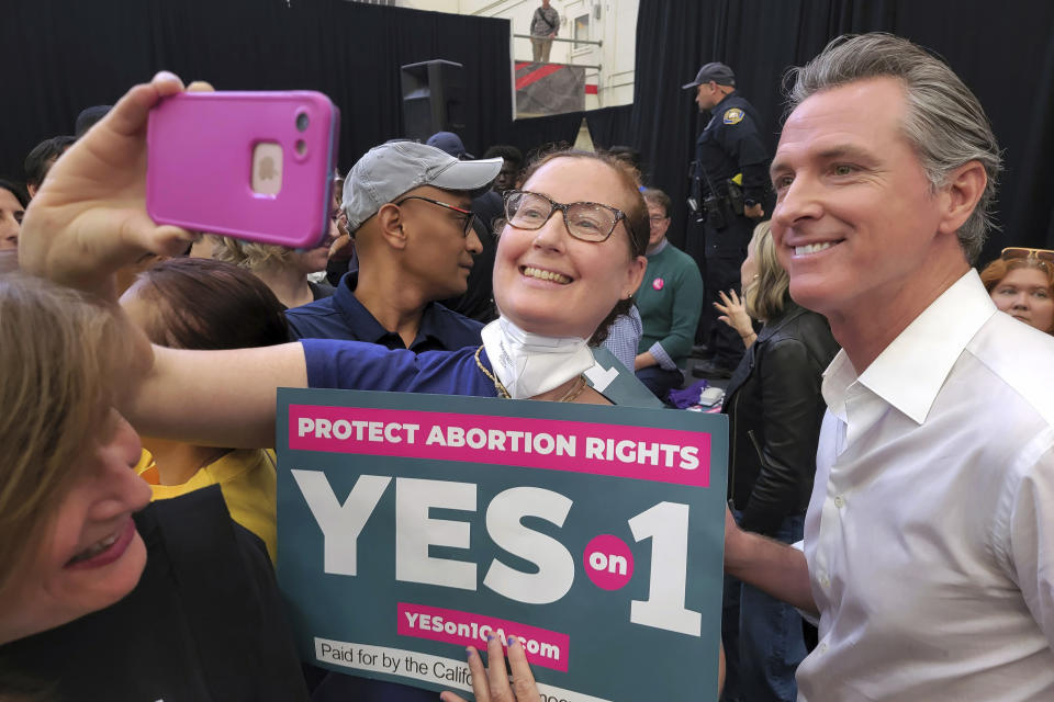 FILE — California Gov. Gavin Newsom, right, takes selfies with supporters at a vote YES on Proposition 1 rally at Long Beach City College in Long Beach, Calif., Nov. 6, 2022. Both Newsom, a Democrat and Florida Gov. Ron DeSantis a Republican said their reelection victories were in part because of their commitment to freedom. But the governors have vastly different definitions of what freedom means. (AP Photo/Damian Dovarganes, File)