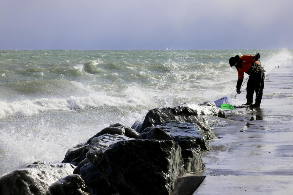 Rae-Ann Eifert, a lake monitor for the Wisconsin Department of Natural Resources, braved sub-freezing temperatures to gather buckets of water for testing off a Lake Michigan breakwater in Racine, Wis., on Feb. 28, 2024, as part of an effort across the Great Lakes to understand the effects of an iceless winter. Unseasonable warmth has left the Great Lakes all but devoid of ice, leaving scientists scrambling to understand the consequences as climate change accelerates. (AP Photo/Teresa Crawford)