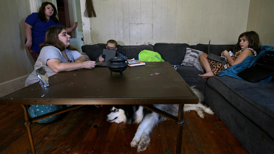 Christi Brouder, left, kneels at a coffee table while helping her children with their lessons, who are remote learning due to the COVID-19 outbreak, in a makeshift classroom in the living room at the family home, Wednesday, Oct. 14, 2020, in Haverhill, Mass. Brouder has four children that are distance learning. Many families with multiple students, some with special needs, are dealing with the challenges of remote distance learning in their home. (AP Photo/Charles Krupa)