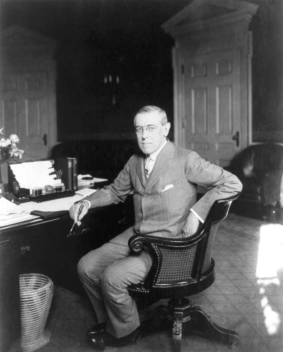 woodrow wilson sitting at a desk, wearing a glasses and gray suit, looking directly into the camera