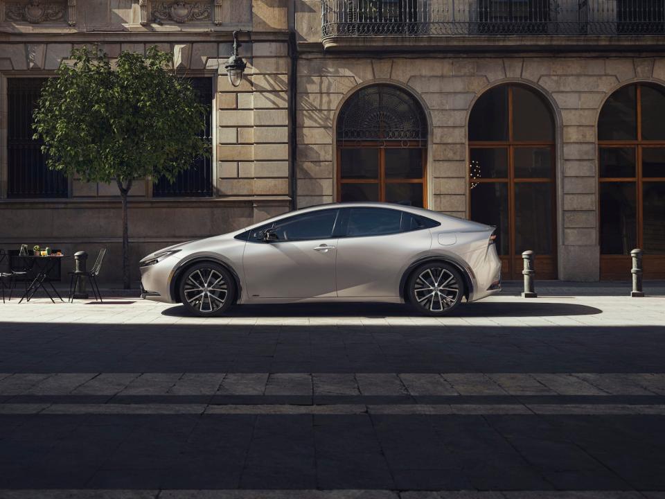 A 2023 Toyota Prius is parked on a city street under a beam of sunlight surrounded by shadows.