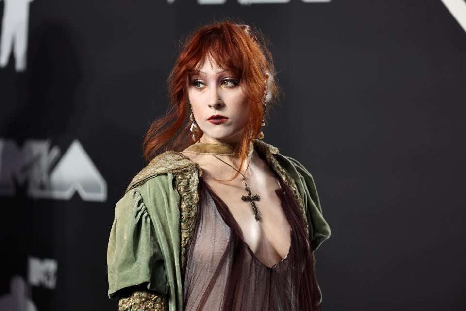 Chappell Roan on the red carpet in a vintage-inspired outfit with a sheer top and an ornate cross necklace at the MTV event