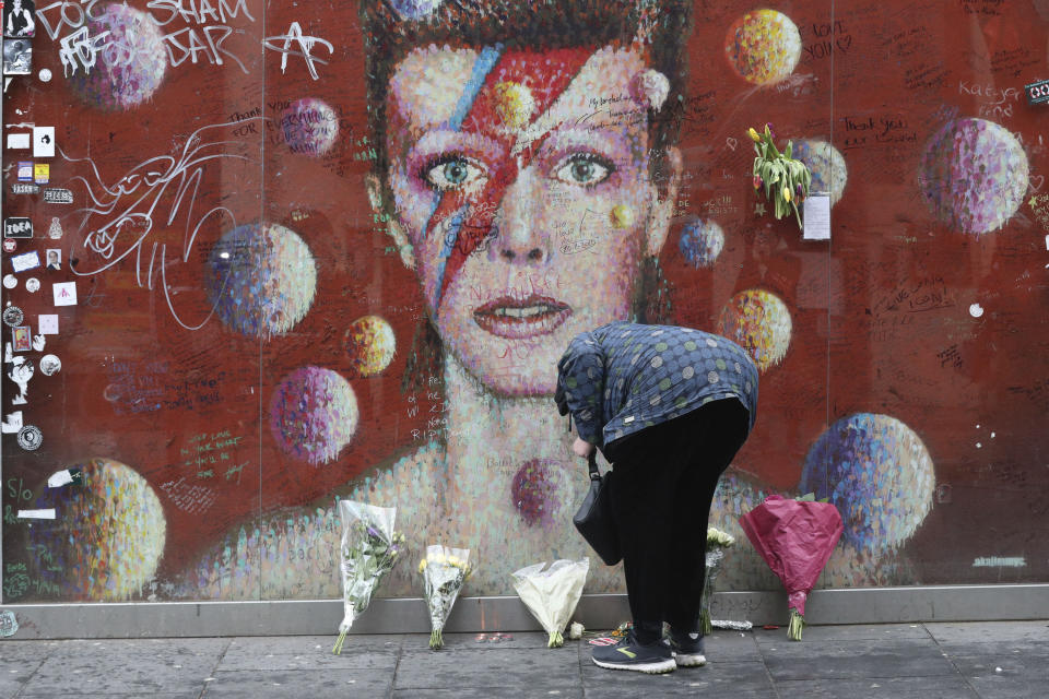 A woman lays a floral tribute at the David Bowie mural in Brixton, south London on the fifth anniversary of the singer's death, Sunday Jan. 10, 2021.  The singer-songwriter Bowie died of liver cancer at his home in New York, USA, on 10 January 2016. (Jonathan Brady/PA via AP)