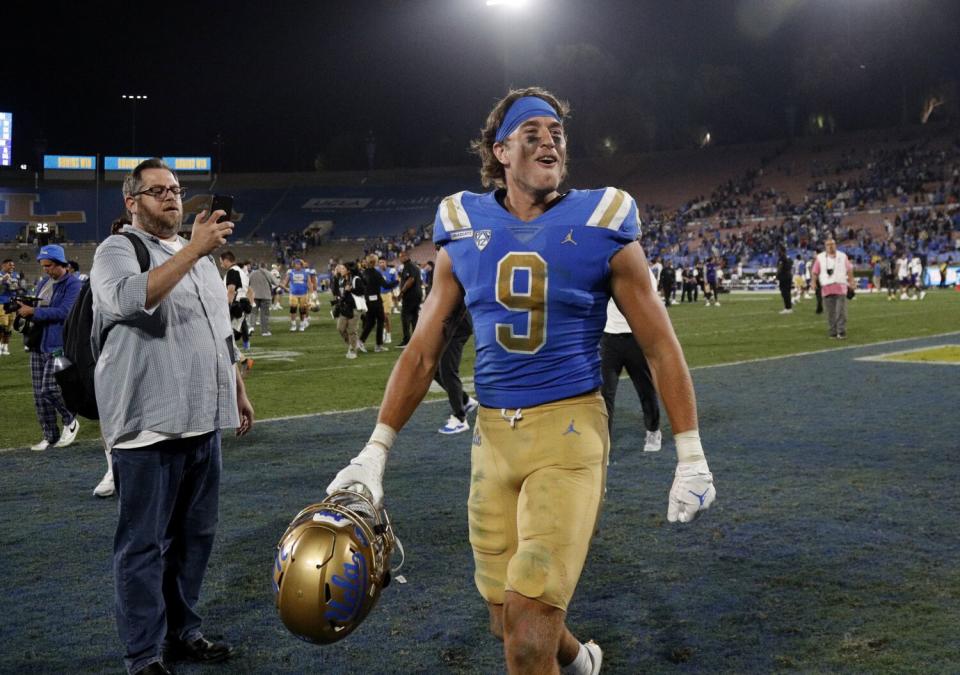 Jake Bobo cheers while holding his helmet and walking in the end zone as a man takes a photo of him.