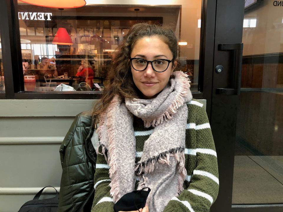 Cristabelle Garcia wearing a green and white striped sweater and scarf sitting in front of a cafe.