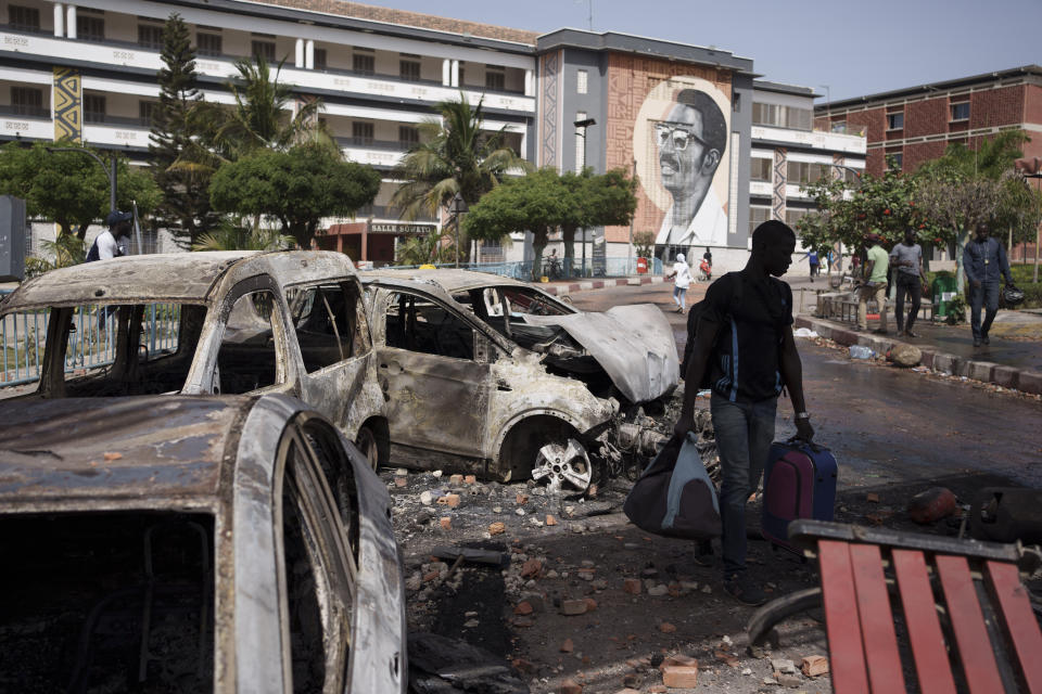 Carrying his belongings a student walks past burned cars as he leaves the Cheikh Anta Diop University after authorities ordered the institution to be closed until further notice in Dakar, Senegal, Friday, June 2, 2023. Clashes between police and supporters of Senegalese opposition leader Ousmane Sonko left nine people dead, the government said Friday, with authorities issuing a blanket ban on the use of several social media platforms in the aftermath of the violence. (AP Photo/Leo Correa)