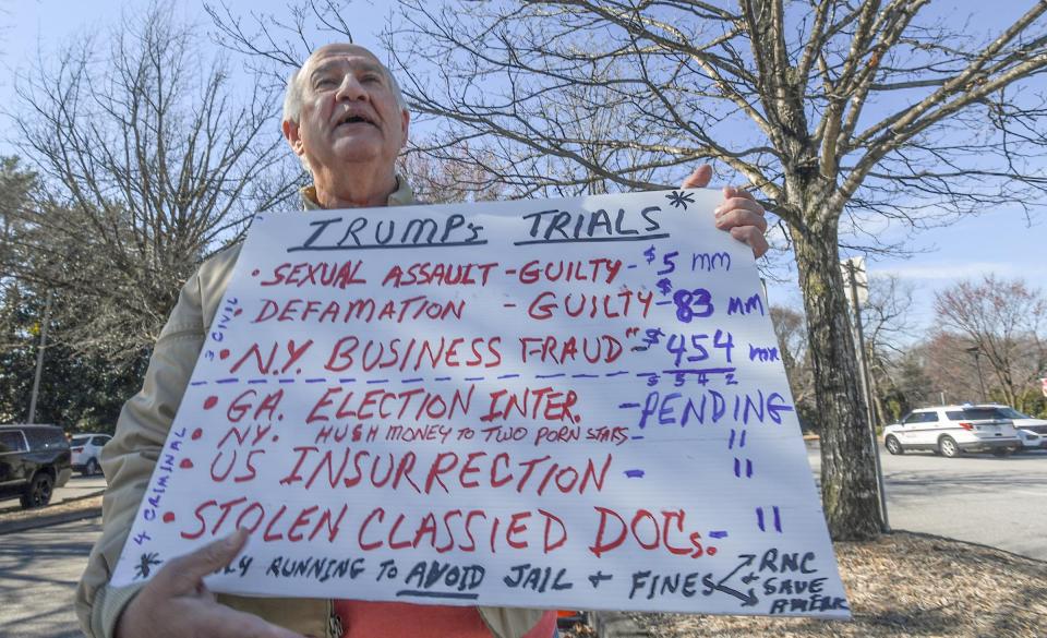 Carl Prestipino of Spartanburg shares his opinion on a two-sided board with concerns about Donald Trump running for U.S. President, across the road from people standing in line for a Trump Town Hall with Fox News at the Greenville Convention Center in Greenville, S.C. Tuesday, February 23, 2024.