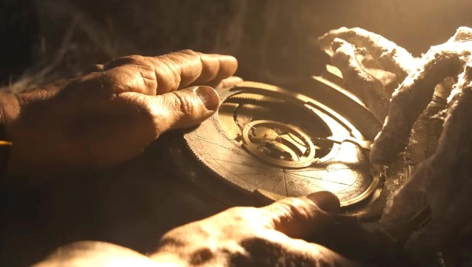 A clock-like device  bathed in light being held by Indiana Jones in The Dial of Destiny