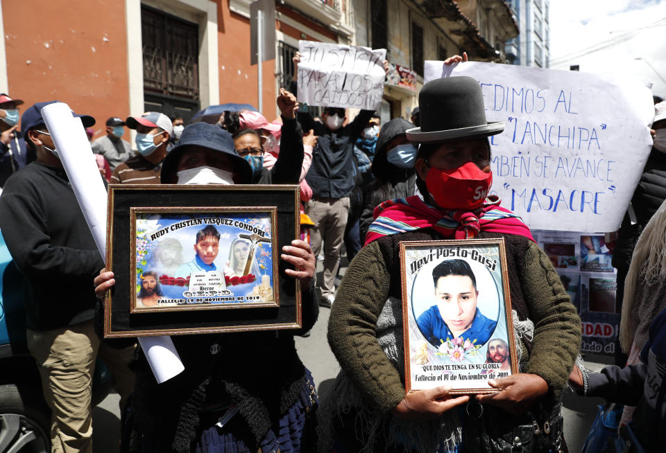 Mujeres sostienen fotografías de fallecidos durante los enfrentamientos ocurridos entre las fuerzas de seguridad y simpatizantes del exmandatario boliviano Evo Morales cuando dirigía el país la expresidenta interina Jeanine Áñez, frente a la comisaría donde se encuentra detenida la exgobernante en La Paz, Bolivia, el domingo 14 de marzo de 2021. (Foto AP/Juan Karita)