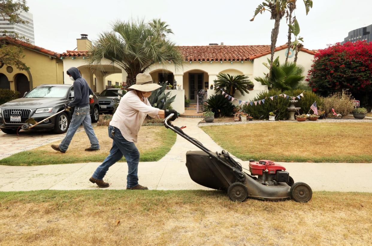 A woman mows a brown lawn.