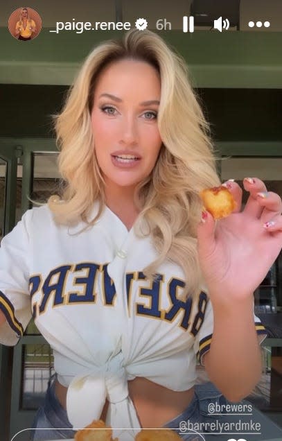Golf social media influencer Paige Spiranac shows off a cheese curd that she had while taste testing food at J. Leinenkugel’s Barrel Yard at American Family Field before the Milwaukee Brewers' game on Friday. She threw out the first pitch and had a bobblehead giveaway.