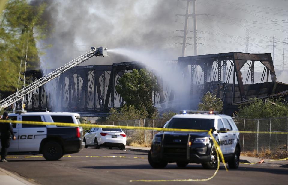 Police cars block off a street as firefighters attempt to put out a fire from a derailed freight train on a bridge spanning Tempe Town Lake Wednesday, July 29, 2020, in Tempe, Ariz. (AP Photo/Ross D. Franklin)