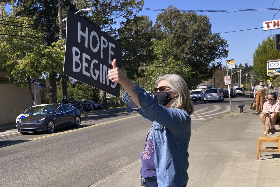 Karen Oneil motions to passing traffic and holds a sign up, with the paint still wet, moments after hearing the guilty verdict of former Minneapolis police Officer Derek Chauvin for the murder of George Floyd, Tuesday, April 20, 2021, in Vashon Island, Wash. A jury convicted Chauvin on murder and manslaughter charges. (AP Photo/Gene Johnson)