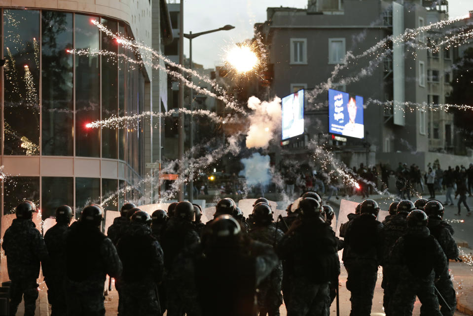 Supporters of the Shiite Hezbollah and Amal Movement groups, background, fire firecrackers against the riot policemen, foreground, as they try to attack the anti-government protesters squares, in downtown Beirut, Lebanon, Saturday, Dec. 14, 2019. Lebanon has been facing its worst economic crisis in decades, amid nationwide protests that began on Oct 17 against the ruling political class which demonstrators accuse of mismanagement and corruption. (AP Photo/Hussein Malla)