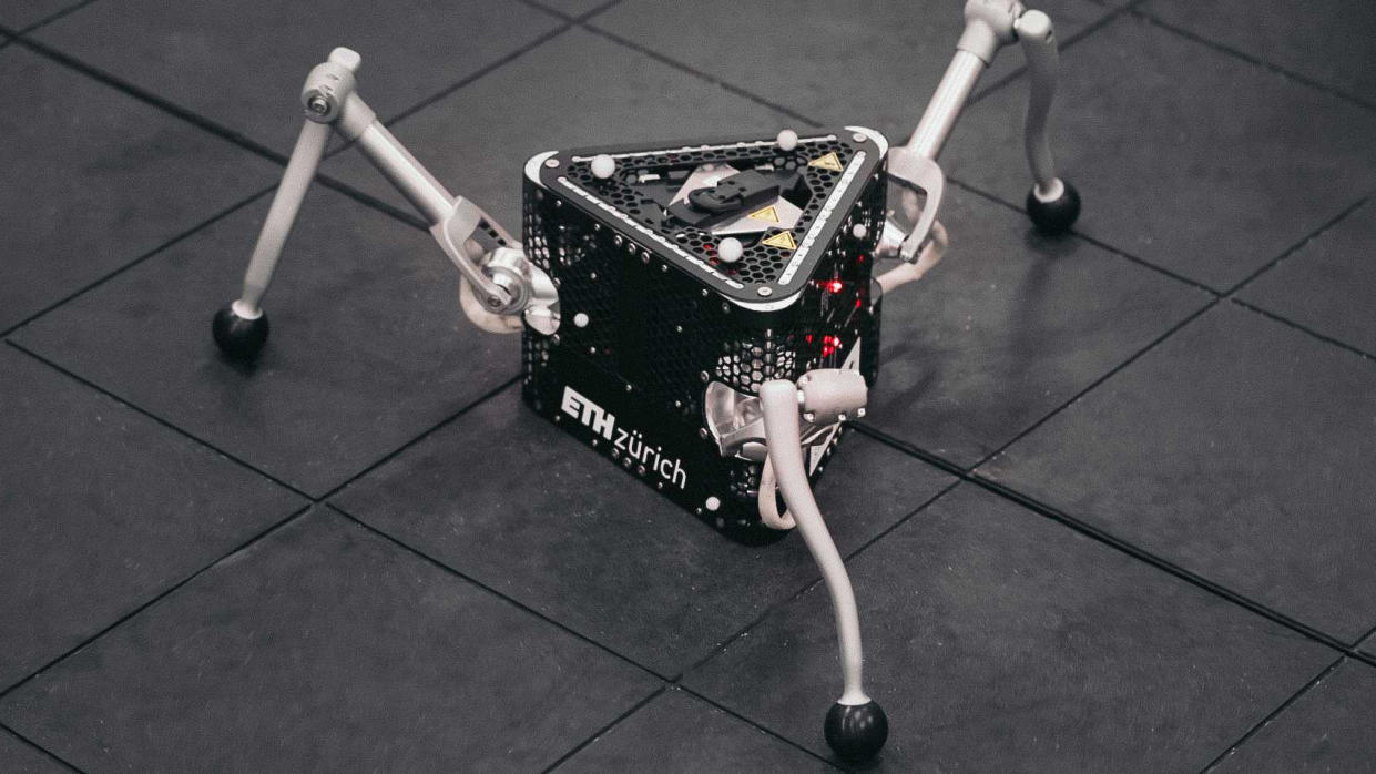  A black prism-shaped robot with three metal grey legs like a spider. 