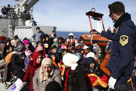 A Greek Coast Guard officer (R) talks to refugees and migrants sitting on the deck of the Agios Efstratios Coast Guard vessel following a rescue operation at open sea between the Turkish coast and the Greek island of Lesbos, in this February 8, 2016 file photo. REUTERS/Giorgos Moutafis/Files