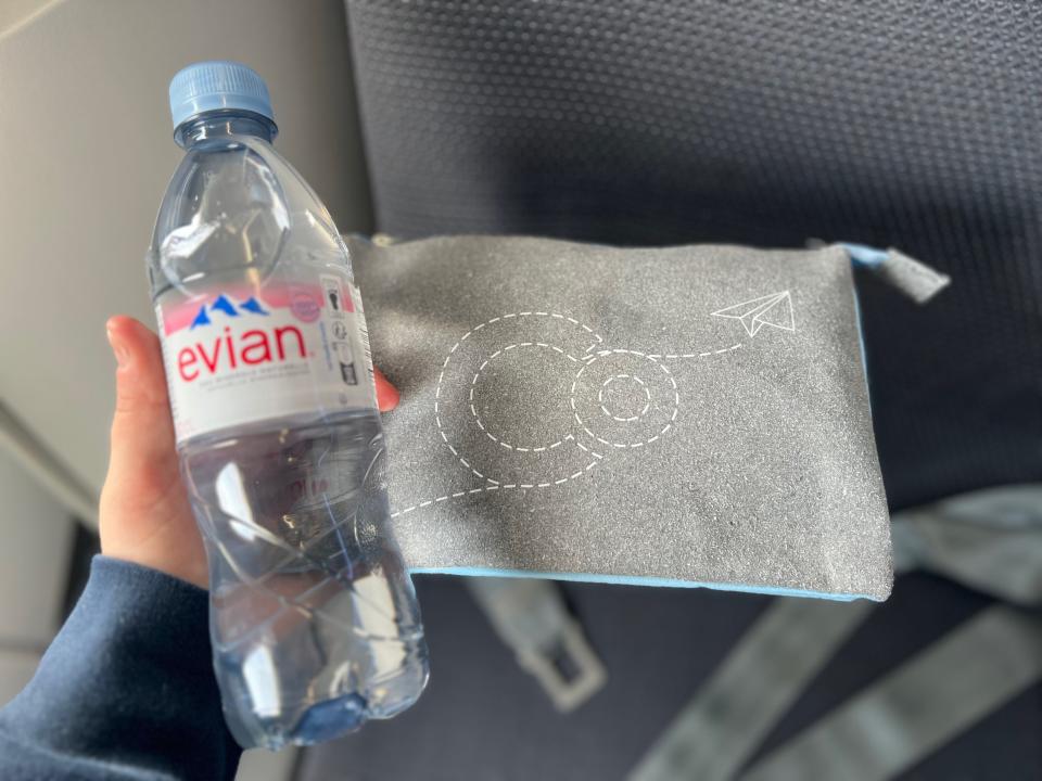 Flying on La Compagnie all-business class airline from Paris to New York — holding the Evian water bottle and La Compagnie-branded amenity kit.