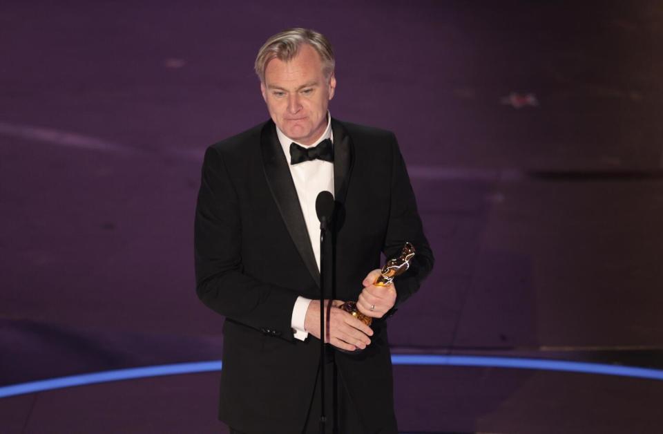 Christopher Nolan holds an Oscar at the mic.